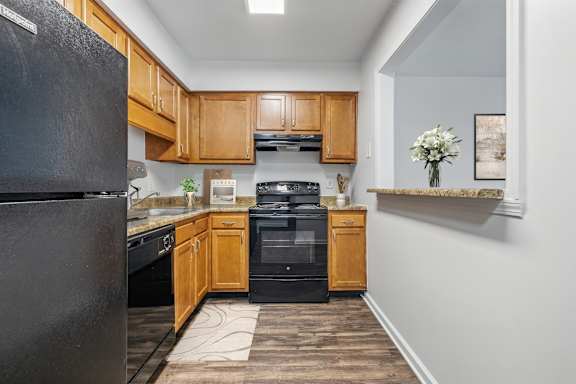 A kitchen with a black fridge, wooden cabinets, and a black oven.
