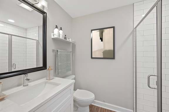A white bathroom with a toilet, sink, mirror, and a picture on the wall. at Indian Creek Apartments*, Cincinnati, OH