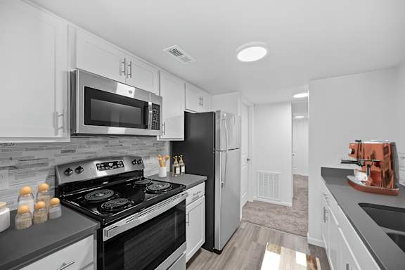 A modern kitchen with black and white appliances and a wooden floor.