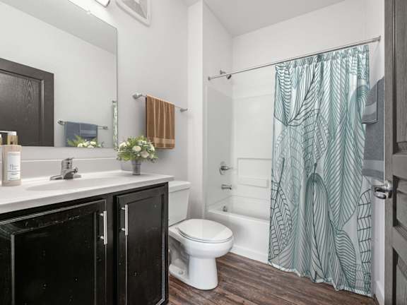 A bathroom with a white toilet, a sink, and a shower with a green curtain. at River View at Bexley Apartments, Ohio