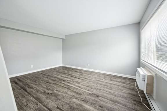 A room with a wooden floor and a window with blinds.