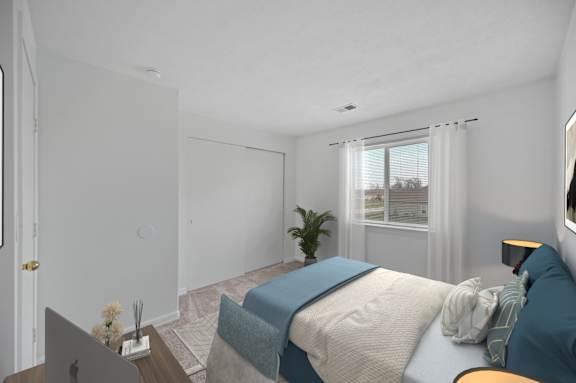 A bedroom with a bed, a desk with a laptop, and a window with curtains.