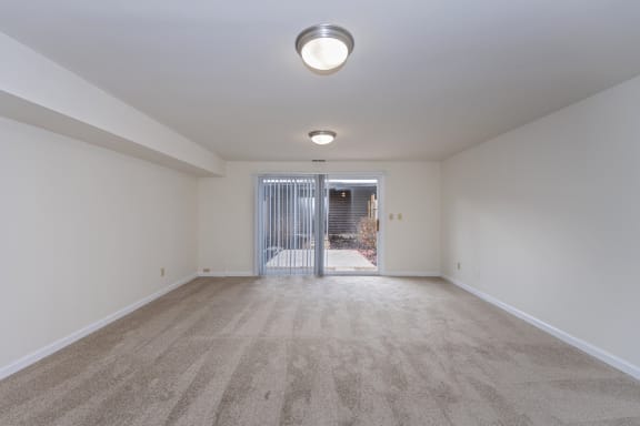 a spacious living room with white walls and carpeting and a door to a balcony at Indian Creek Apartments*, Cincinnati, Ohio