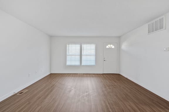 the spacious living room with wood flooring and a door to the bedroom