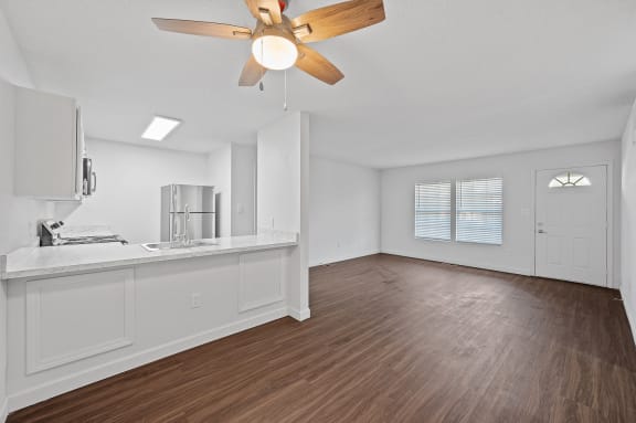 an empty living room with a ceiling fan and a kitchen