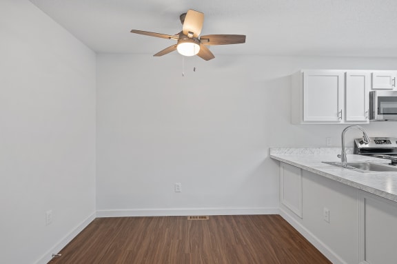 an empty kitchen with white cabinets and a ceiling fan