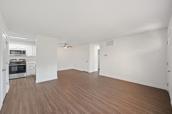an empty living room and kitchen with wood flooring and white walls