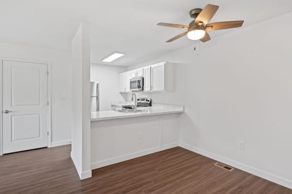 an empty room with a kitchen and a ceiling fan