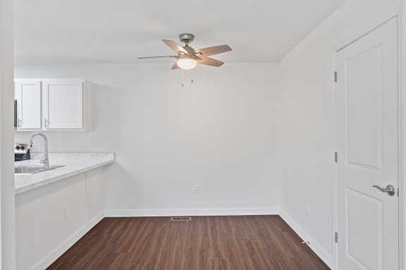 an empty living room with a ceiling fan and a kitchen