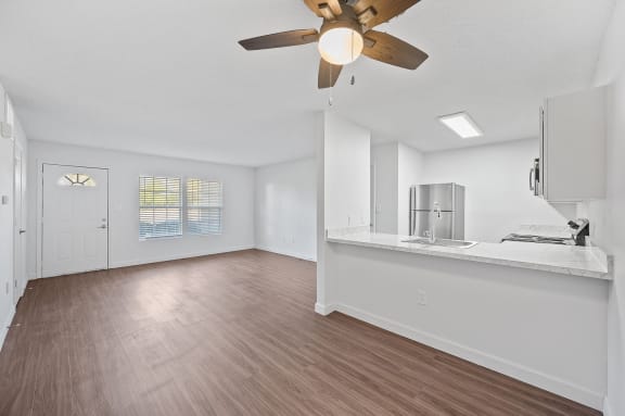 an empty living room and kitchen with a ceiling fan