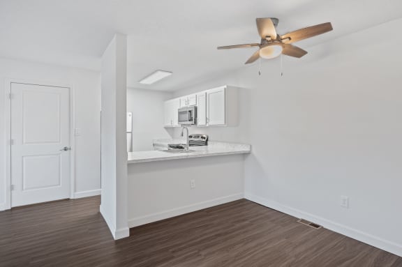 an empty living room with a ceiling fan and a kitchen