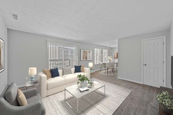 A living room with a grey couch, a glass coffee table, and a dining area in the background.