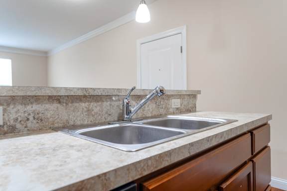 A kitchen sink with a granite countertop and wooden cabinets.