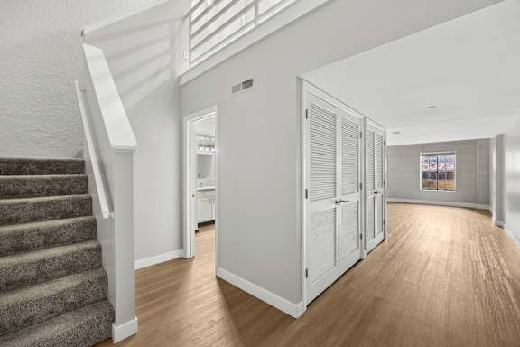 A white interior with a staircase on the left and a doorway leading to another room on the right.