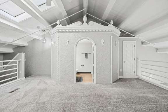 A room with a carpeted floor and a white ceiling with exposed beams.