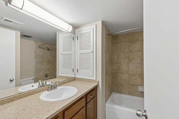 A bathroom with a sink, mirror, and bathtub.