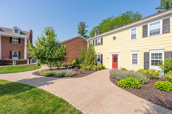 A yellow house with a red door is surrounded by greenery and a concrete pathway. A yellow house with a red door is surrounded by greenery and a concrete pathway. at Indian Creek Apartments*, Ohio