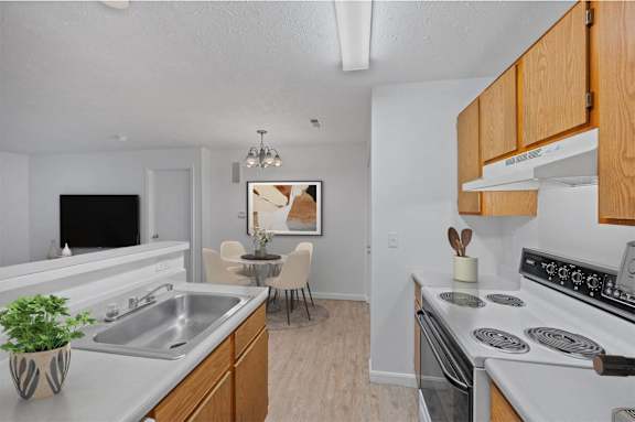 A kitchen with a stove, sink, and a dining table with chairs.