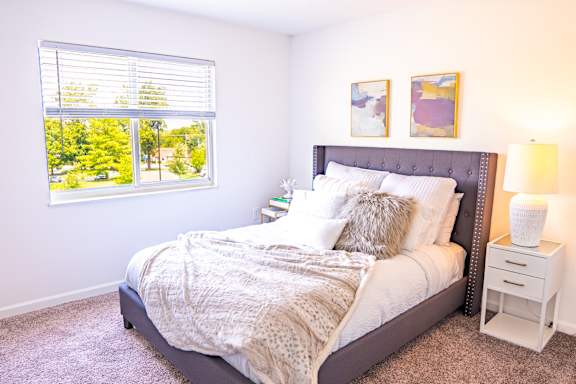 A bedroom with a large bed and a window with blinds.