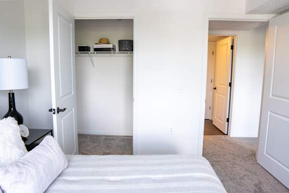 A white bedroom with a bed, lamp, and closet.