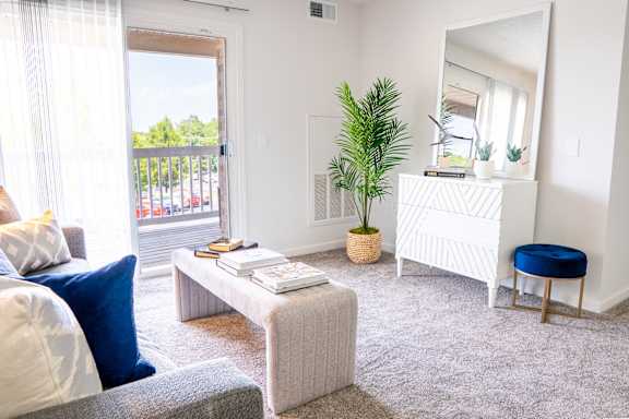 A living room with a white sofa, a grey coffee table, a white side table with a mirror, and a blue stool.