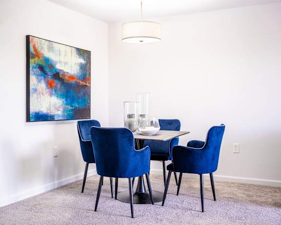 A dining room with a large painting on the wall and a table with chairs.