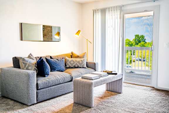 A grey couch with blue pillows and a grey coffee table in a room with a large window.