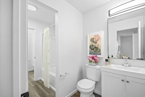 A white bathroom with a toilet, sink, and a painting of flowers.