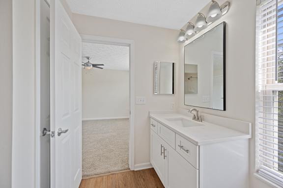 A white bathroom with a sink, mirror, and a fan.