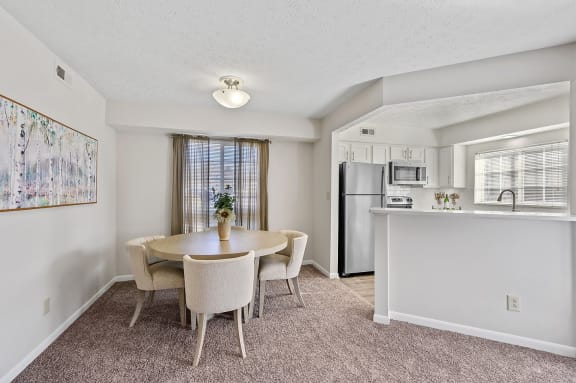 a dining area with a table and chairs and a kitchen with a refrigerator