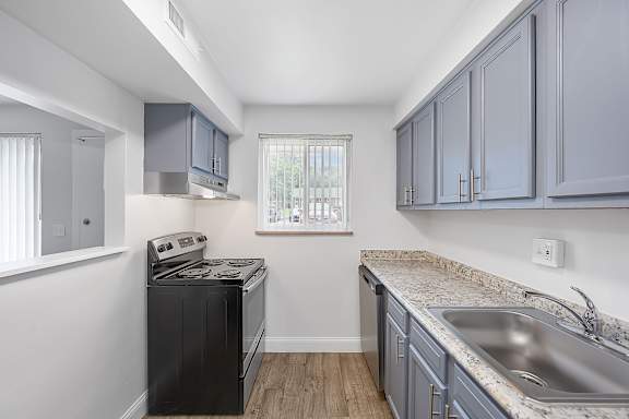 A kitchen with a black dishwasher and grey cabinets.