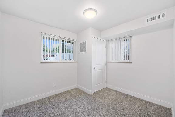 A room with a carpeted floor and a window with blinds.