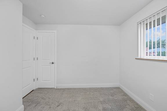A white room with a carpeted floor and a window with blinds.