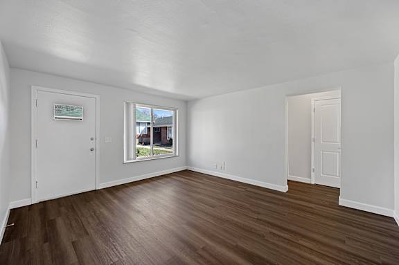 A room with white walls and wooden flooring with a window.