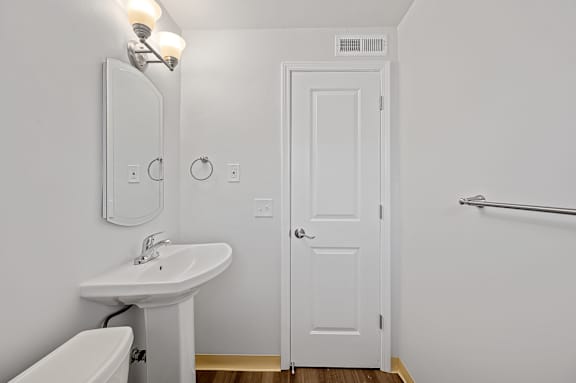 A white bathroom with a toilet, sink, mirror, and door.