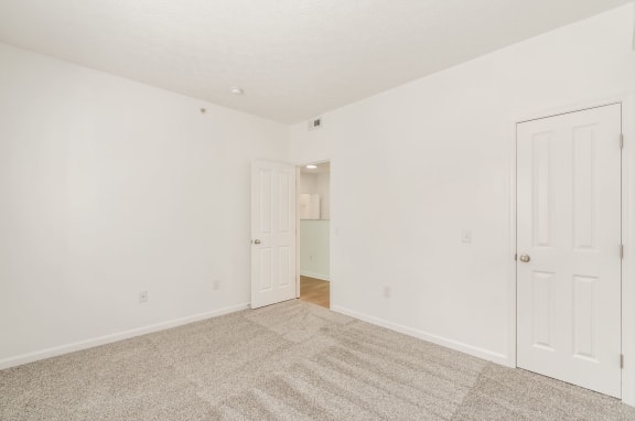 a bedroom with white walls and carpet and a door to a closet