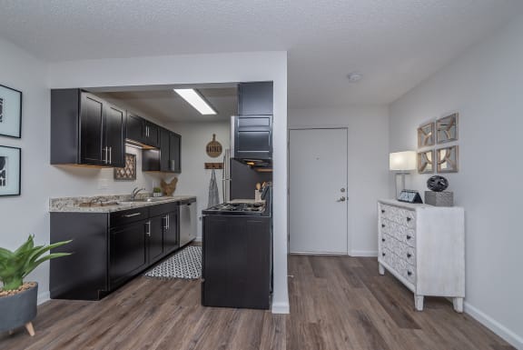 an open kitchen and living room with black appliances and wood flooring