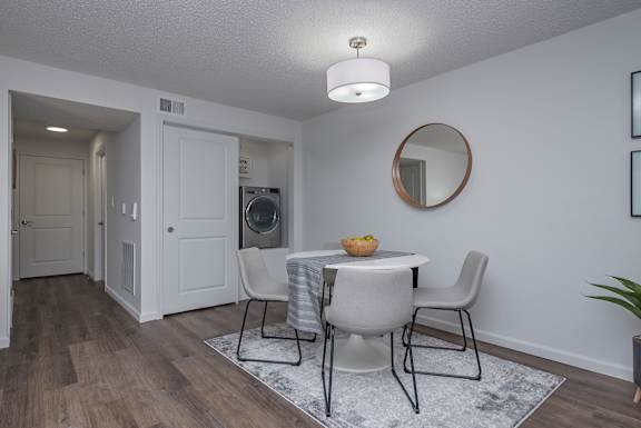 A dining room with a round mirror and a table with chairs.