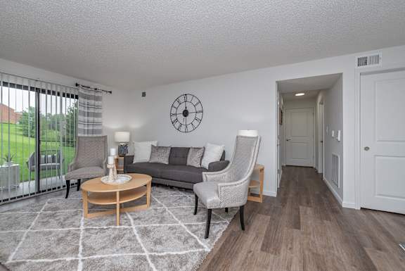 A living room with a grey couch, a wooden coffee table, and a large clock on the wall.