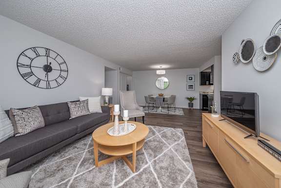A living room with a grey couch, a wooden coffee table, and a large clock on the wall.