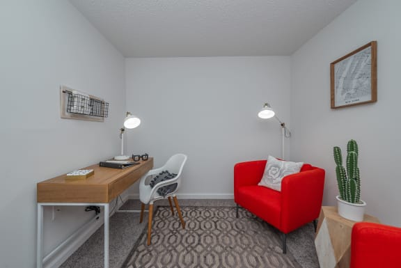 a living room with a red chair and a desk with a cactus