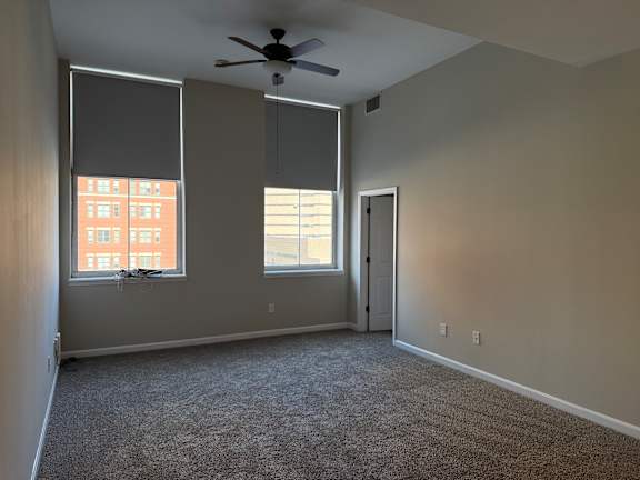 A room with a ceiling fan and two windows.