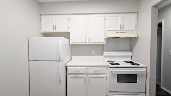 A white kitchen with a refrigerator, stove, and cabinets.