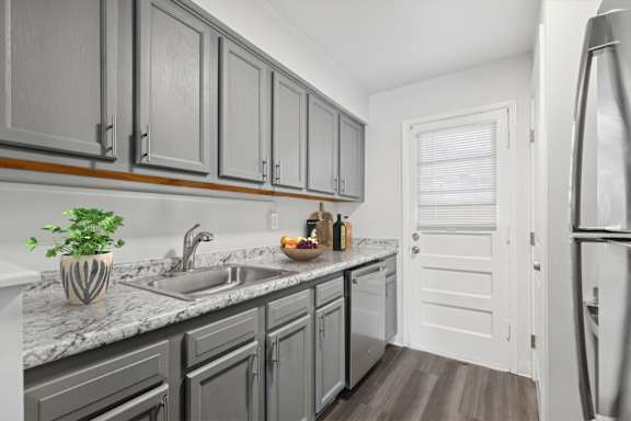 A kitchen with a marble countertop and grey cabinets.