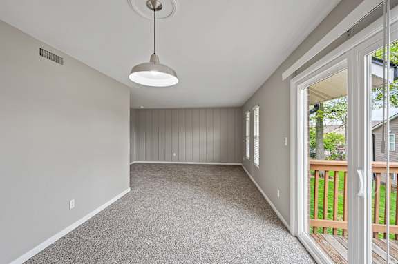 A room with a grey carpet and a hanging light fixture.