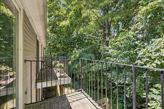 A balcony with a railing overlooks a wooded area.