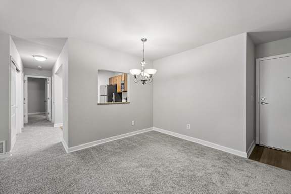 A spacious room with a grey carpet and a chandelier hanging from the ceiling.