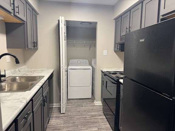 A black refrigerator is on the right side of a kitchen at Quail Run Apartments, Columbus, IN
