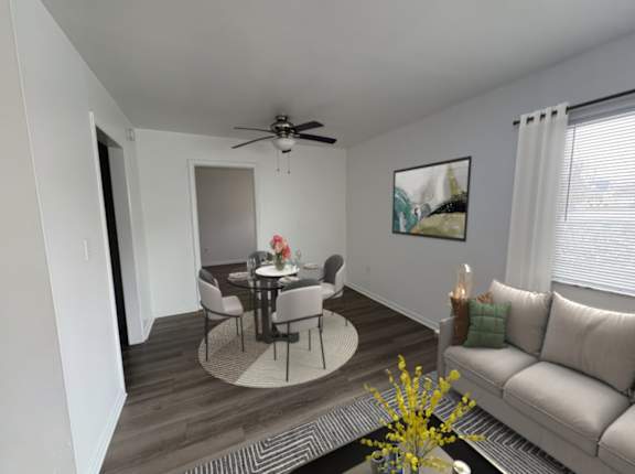 A living room with a grey couch, a round table with four chairs, a ceiling fan, and a painting on the wall.