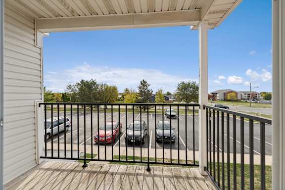 A balcony with a black railing and a view of cars and trees.